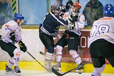 Zwei Eishockeyspieler kollidieren während eines Spiels nahe der Bande, einer der Black Dragons Erfurt (dunkles Trikot) und ein Gegenspieler (helles Trikot). Eis spritzt um ihre Schlittschuhe, während ein weiterer Spieler im Hintergrund beobachtet.
